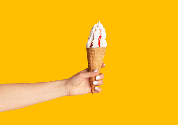 Giovane ragazza che tiene il gelato gustoso con bacca topping in cono cialda su sfondo arancione, primo piano di mano
 - Foto, immagini
