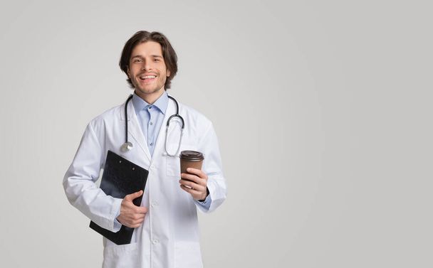 Портрет молодого улыбающегося врача с медицинской картой и кофе на вынос
 - Фото, изображение
