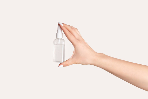 Prevenzione delle infezioni virali. Giovane donna in possesso di bottiglia con igienizzante su sfondo chiaro, primo piano
 - Foto, immagini