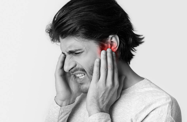 Człowiek cierpi na ból ucha. Dotykając dłońmi jego bolesnej głowy - Zdjęcie, obraz