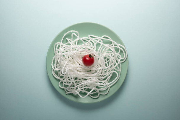 White rope with red tomato on a round plate. Spaghetti concept - Zdjęcie, obraz