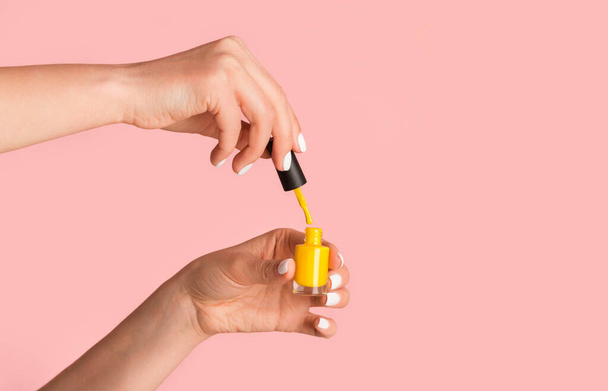 Close up of nail artist holding bottle of yellow enamel on pink background, copy space - Zdjęcie, obraz