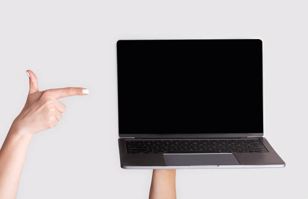 Menina irreconhecível apontando para o computador portátil com tela vazia para o seu design, fundo claro. Panorama
 - Foto, Imagem