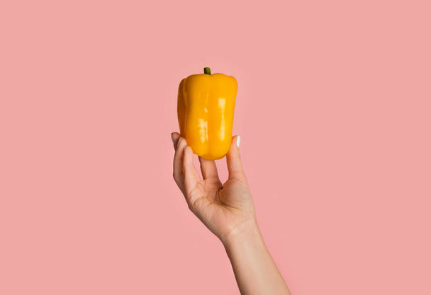 Eat vegan concept. Millennial girl showing yellow bell pepper on pink background, closeup - Photo, image