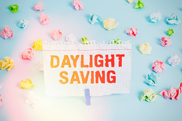 Text sign showing Daylight Saving. Conceptual photo Storage technologies that can be used to protect data Colored crumpled papers empty reminder blue floor background clothespin. - Photo, Image