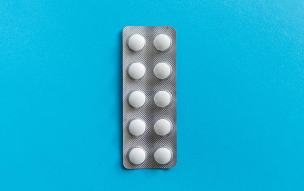 Top view on the pills in the package. White pills on blue background. Medicine, medication, painkillers, tablet, medicaments, drugs, antibiotic, vitamin, treatment, capsule, dose. Pharmacy theme. - Foto, immagini