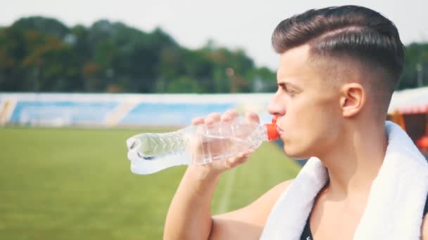 Young handsome sportman is finishing his training on the stadium and drinking water. Side view. Close up. Copy space. 4K. - Záběry, video