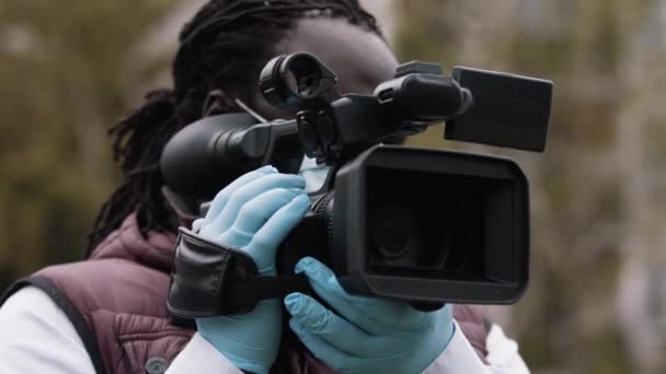 Afrikanischer Reporter hält die Kamera mit den Latexhandschuhen. Berichterstattung über Covid-19-Ausbruch - Filmmaterial, Video