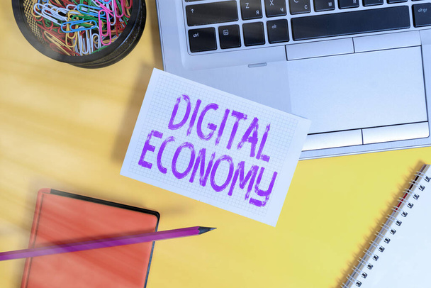 Text sign showing Digital Economy. Conceptual photo worldwide network of economic activities and technologies Laptop pencil sheet clips container spiral notebook colored background. - Photo, Image