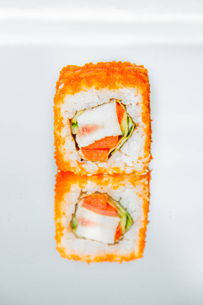 Un hermoso y delicioso rollo de sushi se encuentra en una mesa de espejo y se refleja en él
. - Foto, Imagen