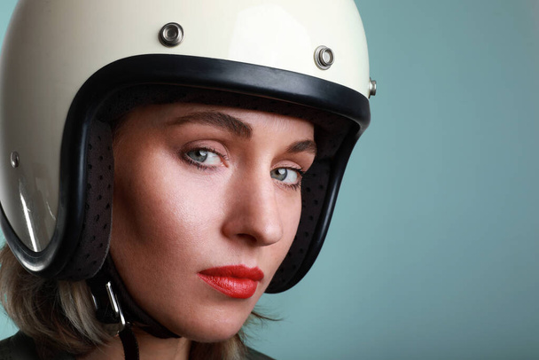 Close-up portrait of biker young woman, wearing white helmet, with red lips. Studio blue background. Space for your text. - Foto, Imagem