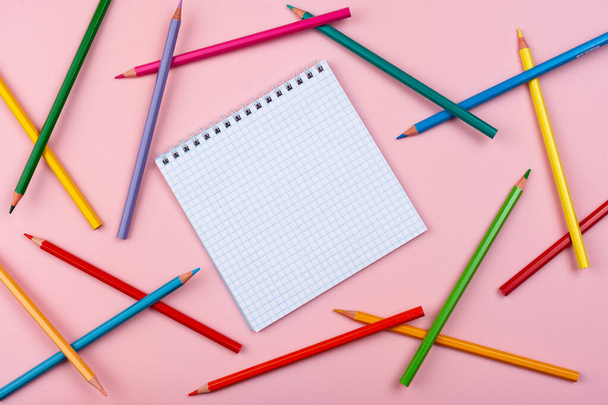 notebook on a pink background. Colored pencils are scattered nearby. - Zdjęcie, obraz