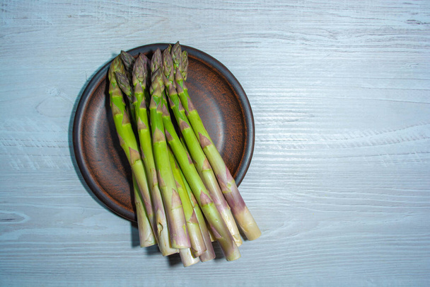Asparagus on a clay plate. A bunch of asparagus shoots on a clay plate and on a gray wooden background - Fotó, kép