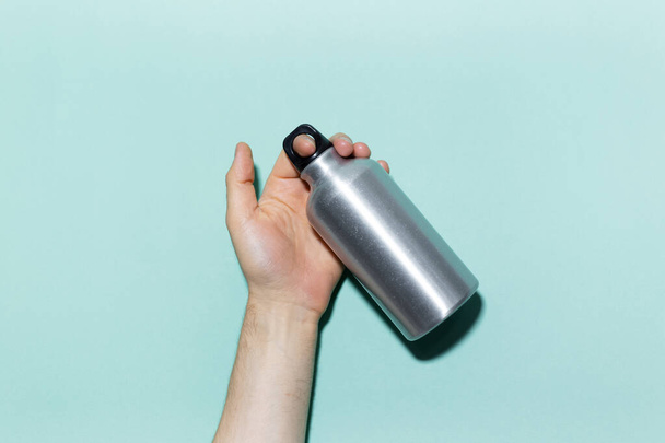 Close-up of male hand holding eco, reusable aluminum thermo water bottle on studio background of cyan, aqua menthe color. - Foto, immagini