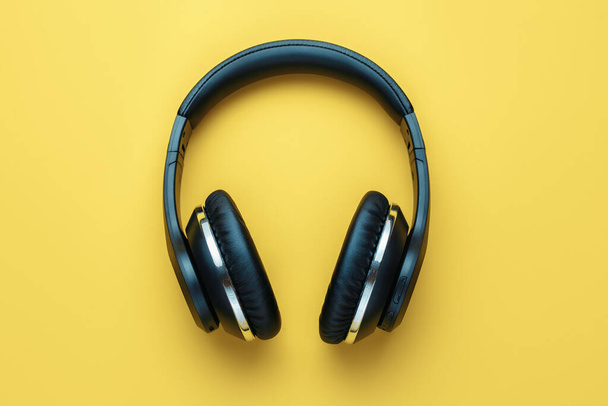 Photo of black stylish modern wireless headphone in neon lights over yellow background. - Fotó, kép