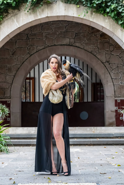 A gorgeous Hispanic Brunette model poses outdoors with a Caracara bird outdoors at a hacienda - Foto, immagini