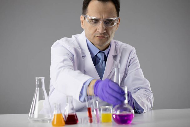 Ερευνητής χημικός επιλέγει φιάλες γεμάτες πολύχρωμα χημικά διαλύματα - Φωτογραφία, εικόνα