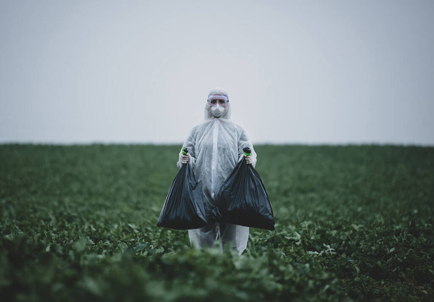 medic in a protective suit collects with two bags in green field  - Fotografie, Obrázek