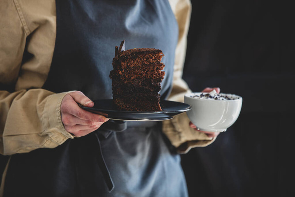 femme dans un tablier tient cappuccino et gâteau au chocolat
  - Photo, image