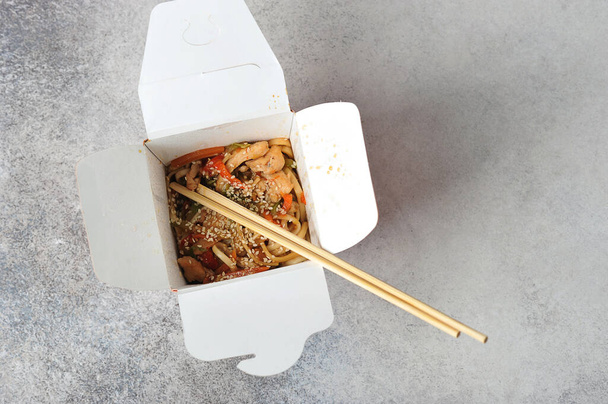 Chinese noodles in paper packaging with chopsticks on a gray background - Japanese cuisine-top view - 写真・画像
