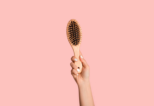 Closeup of millennial girl holding wooden hairbrush on pink background - Fotó, kép