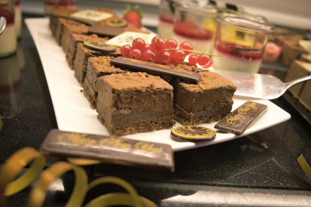 Закрытие десертного шведского стола на Новый год. Шоколадный торт с красной смородиной и фруктовым муссом в очках. Четвёртый размер. Ряд индивидуальной подачи десертов
. - Фото, изображение
