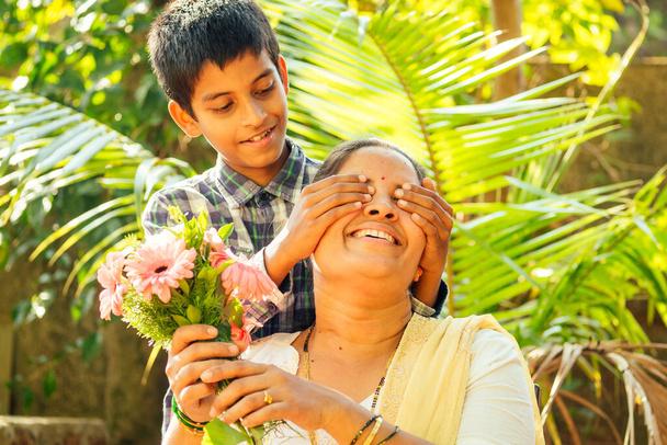 indian little boy holding bouquet and making surprise for his mother outdoor in park - 写真・画像