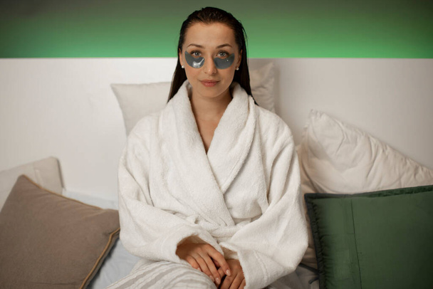 Mooi rustig meisje ontspannen in badjas en hydraterende cosmetische ooglapjes - Foto, afbeelding