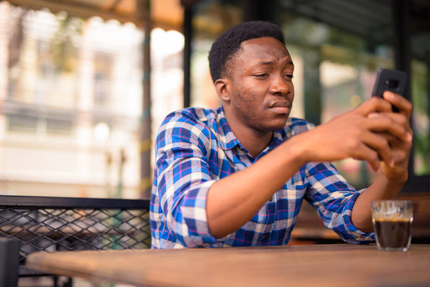 Portrait of young handsome African man relaxing at the coffee shop - Foto, immagini