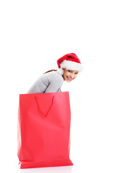Beautiful girl wearing santa hat in red shopping bag. - Фото, изображение