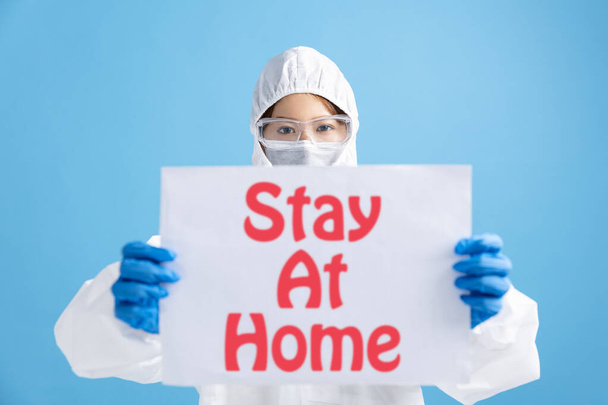 Krankenschwester mit Schutzbrille und weißem Schutzanzug. Werbetafel zeigt Aufenthalt zu Hause - Foto, Bild