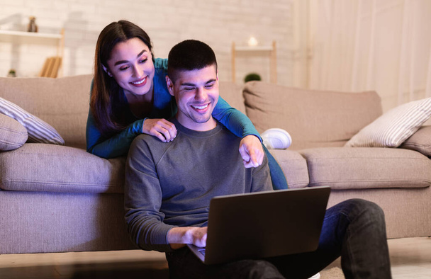 Happy couple using pc sitting in cozy living room - Foto, afbeelding