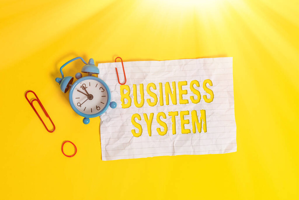 Writing note showing Business System. Business photo showcasing A method of analyzing the information of organizations Metal alarm clock blank crushed note rubber band colored background. - Photo, Image