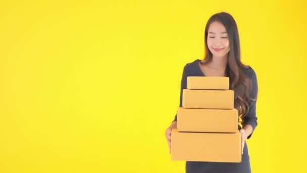 πλάνα από όμορφη ασιατική γυναίκα κρατώντας στοίβα από κουτιά που απομονώνονται σε κίτρινο - Πλάνα, βίντεο