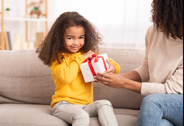 Девушка распаковывает подарок сидя с мамой на диване дома
 - Фото, изображение