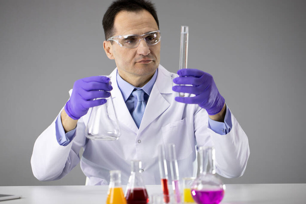 Inteligentny naukowiec w okularach ochronnych pracuje w laboratorium chemicznym z lampami reakcyjnymi - Zdjęcie, obraz