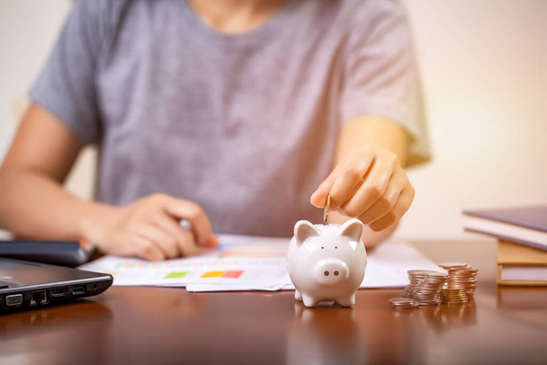 Female hand putting money into piggy bank for saving money, write finance. - Photo, Image
