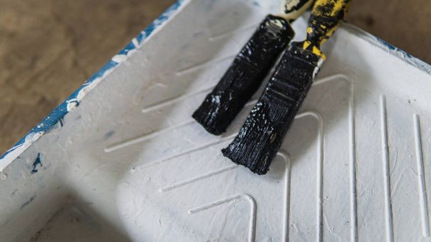 Két szárított ecset fekete festékkel egy műanyag fehér festőtálcán. Szelektív szög és fókusz. Művészeti koncepció. - Fotó, kép