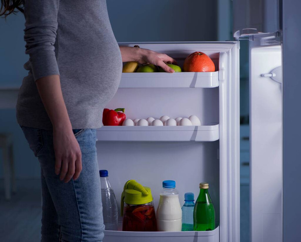 Pregnant woman near fridge looking for food and snacks at night - Fotó, kép