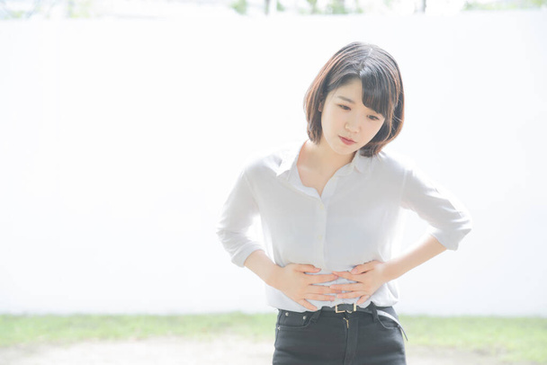 Jeune femme asiatique tenant les mains avec douleur dans l'abdomen à l'extérieur
 - Photo, image