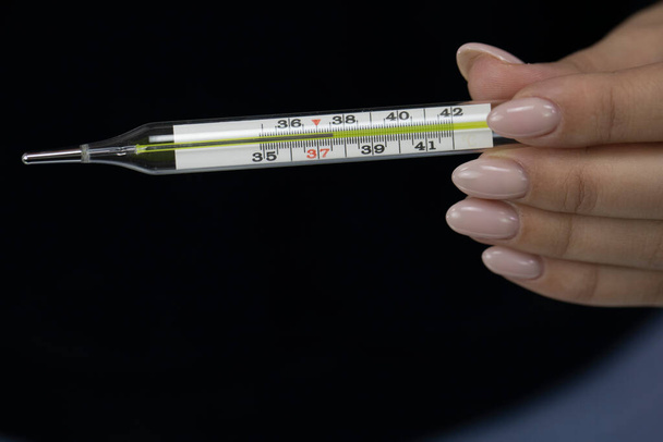 Weibchen hält Quecksilberthermometer in der Hand, das 37,6 Grad anzeigt - Foto, Bild