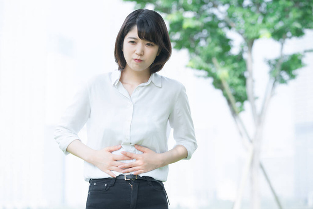 Nuori aasialainen nainen kädestä vatsakipu ulkona
 - Valokuva, kuva