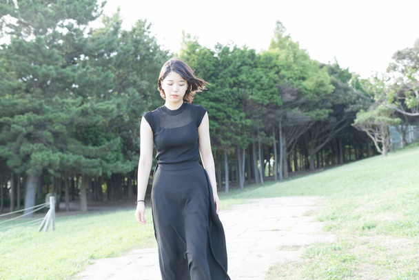 Азиатская (японская) молодая женщина в черном платье в парке у моря
 - Фото, изображение