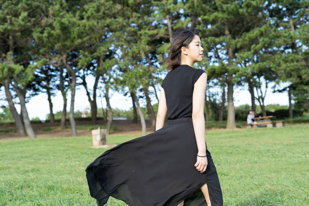 Азиатская (японская) молодая женщина в черном платье в парке у моря
 - Фото, изображение
