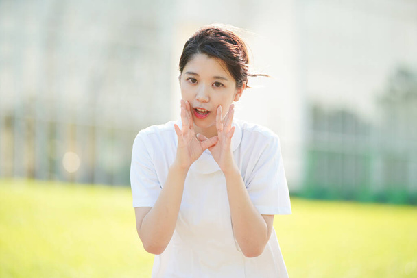Una enfermera asiática (japonesa) que posa para animar con la mano en la boca
 - Foto, imagen