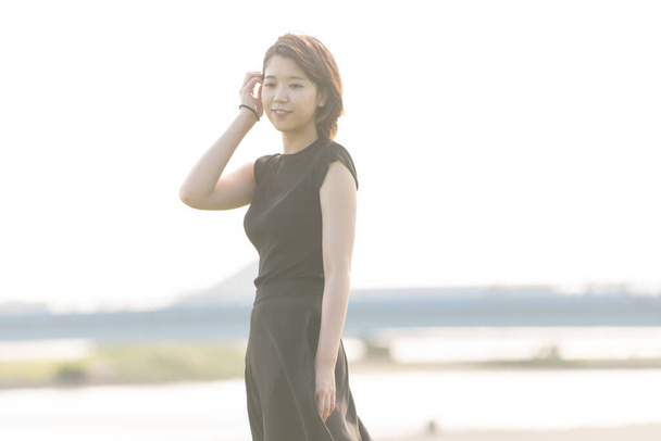 Азійська (японська) молода жінка в чорній сукні в парку біля моря. - Фото, зображення