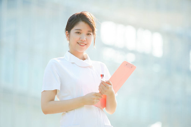 Портрет азиатской (японской) медсестры с улыбкой на открытом воздухе
 - Фото, изображение