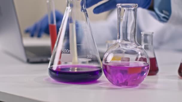 Close up lab glassware with colorful liquids, scientist works on background - Footage, Video