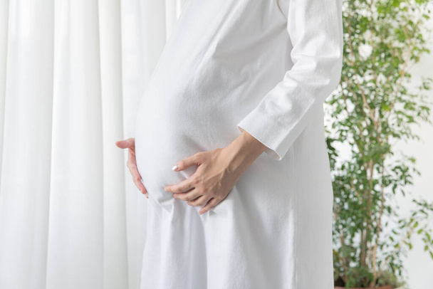 Asijské (japonská) mladá těhotná žena v bílých šatech dotýká břicho - Fotografie, Obrázek