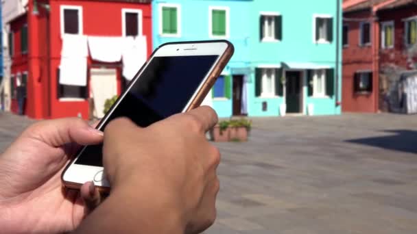 4K, Closeup of asian hands using smartphone in street of Burano island with beautiful and colourfully painted houses in background. Woman holding a cell phone and touch screen for surfing internet-Dan - Footage, Video
